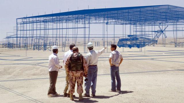 Five men standing outside looking at a 3D rendering of a hangar and helicoprter