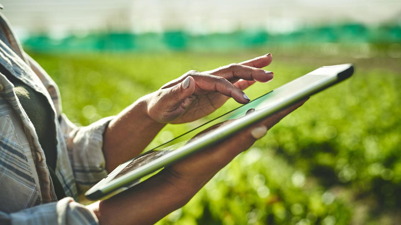Shot of a woman's hand using a tablet in front of a farm