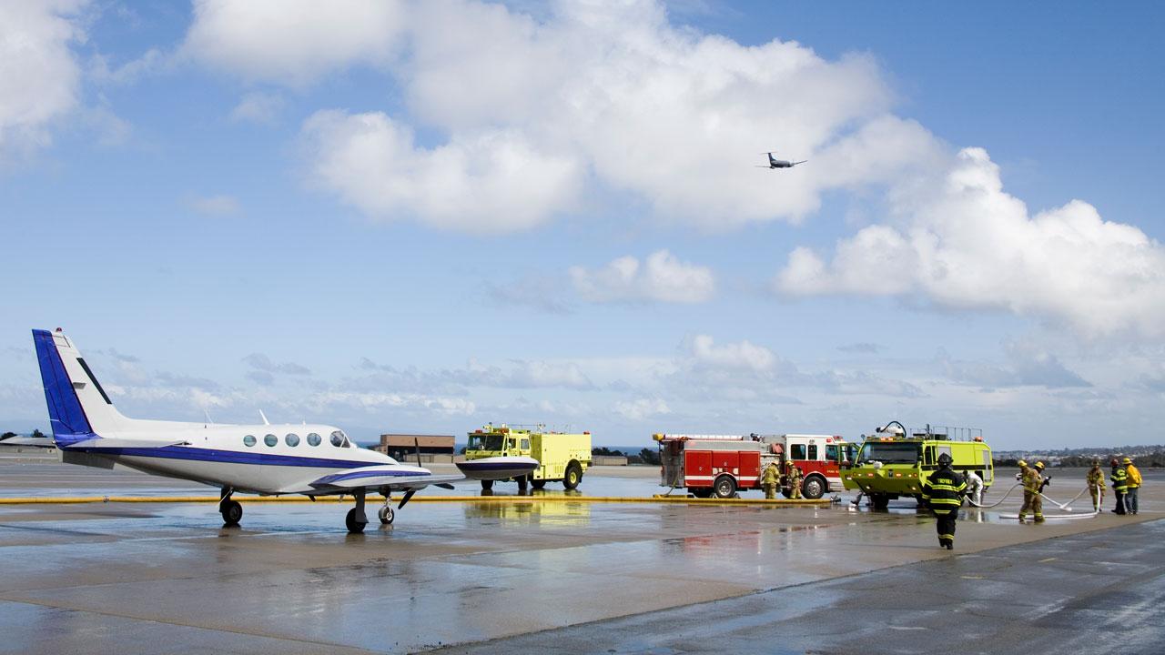 消防车和消防队员在停机坪上与一架小飞机在广阔的蓝天下与蓬松的云