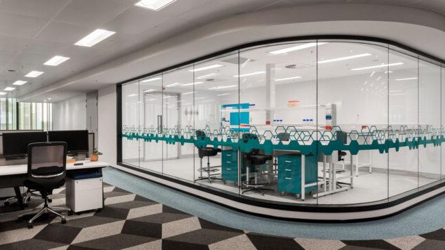 A small lab space within an office floor. The lab space is separated by a curved glass wall