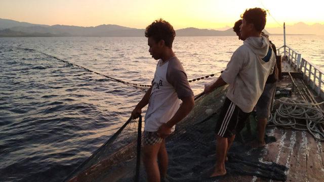 Three Indonesian fishermen cast a net while fishing offshore